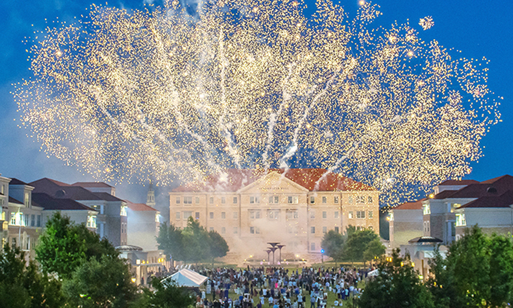 A large shower of golden fireworks light up the sky above a crowd of students