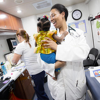 Medical student holding a baby In an examination room, a smiing medical school student with a stethoscope around her neck holds a baby