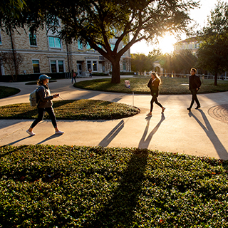 TCU students wearing jackets walk on campus, casting long shadows on a sunny day TCU students wearing jackets walk on campus, casting long shadows on a sunny day