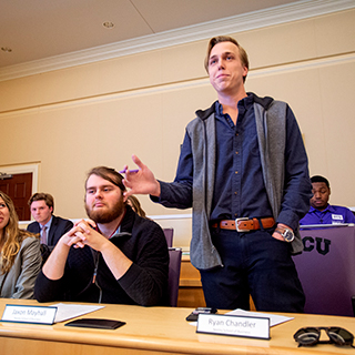A male student stands to speak at a TCU student government meeting in the chambers of the student union. A male student stands to speak at a TCU student government meeting in the chambers of the student union.