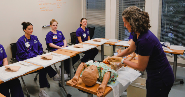 Medical students watch an instructor demonstrate a procedure using a pediatric patient simulator
