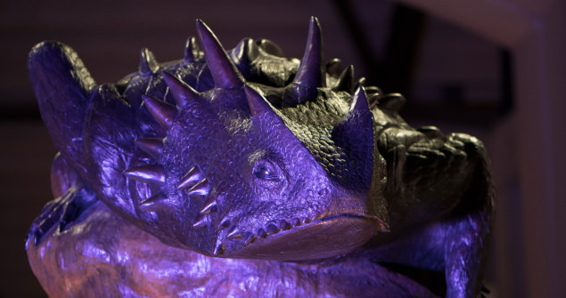Bronze sculpture of a horned lizard, bathed in purple light