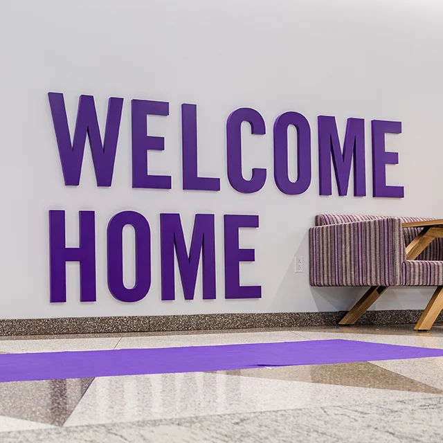 Students in purple shirts walk past a Welcome Home lobby sign