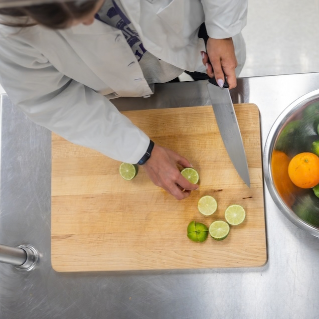 Two occupational therapy students in white coats prepare fresh produce, including limes, onions and celery, as part of lifestyle medicine training.